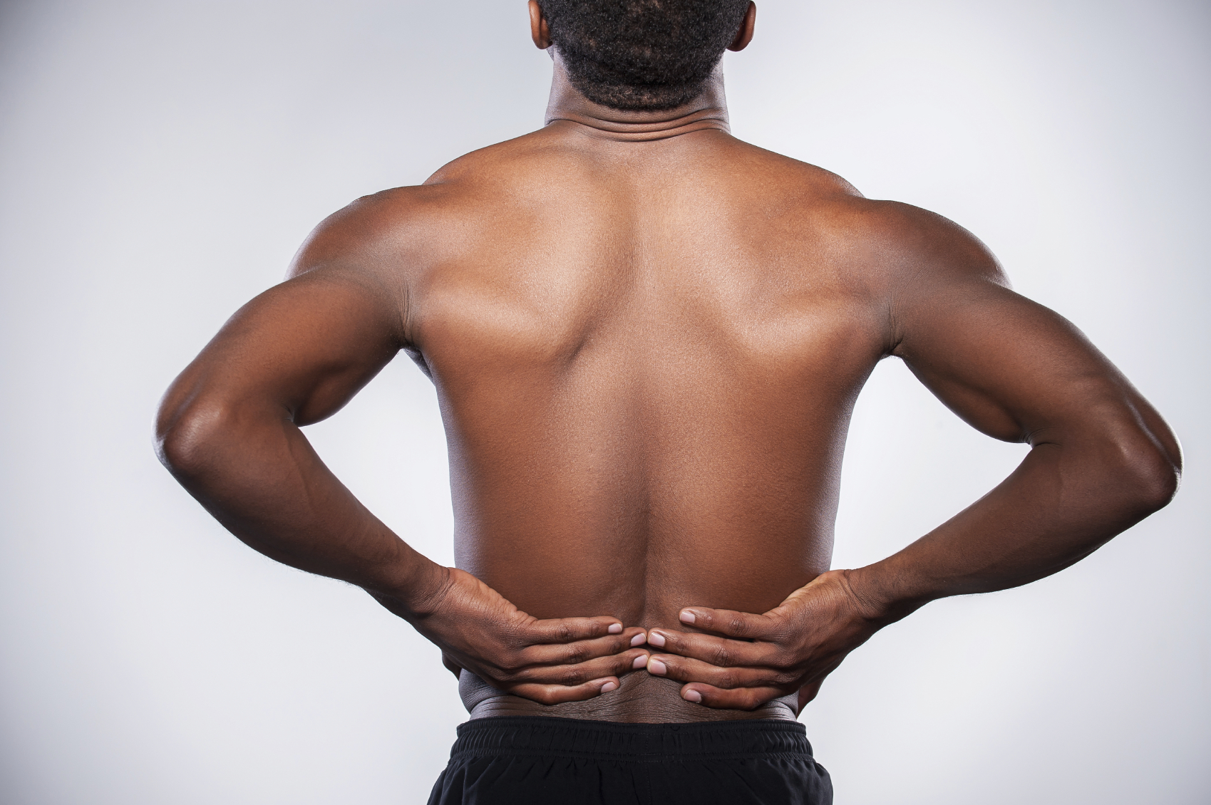 Backache. Rear view of young muscular African man touching his hip while standing against grey background